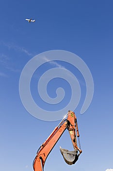 Orange excavator and airplane on blue sky background