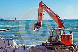 Orange excavator on the beach of the French city of Cannes against the background of the blue sea.