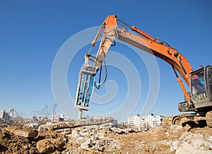 Orange excavator with an industrial hydraulic hammer against a blue sky