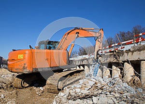 Orange excavator with an industrial hydraulic hammer is working on a construction site