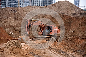 Orange excavator machine on earthworks in sandpit at construction site. Backhoe digs ground for construct foundantion