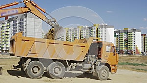 Orange excavator pours the soil into the dump truck in slow motion. Construction of a residential multi-apartment