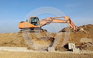 Orange excavator during a road work on a dirt heap with blue sky background.