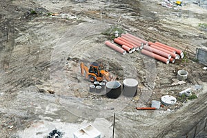 Orange excavator standing on a ground during construction of a new building in the city area. Aerial view on a