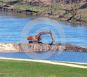 Orange excavator works on the river bank