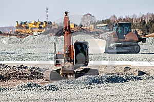 Orange excavator and yellow bulldozer dredges rubble at road construction