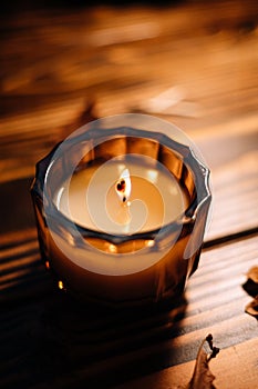 Orange fall candle resting on a wooden surface, surrounded by feathers