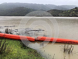 Orange floating debris boom, barrier on the green grass and in the water of a full reservoir during the rainy season