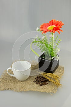Orange flower in a vase with coffee cup on gunny textile isolate