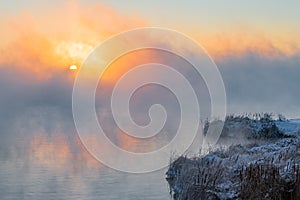 An orange fog spreads over the water and obscures the horizon.  Sunset Sunrise time over the winter river