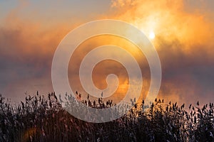 An orange fog spreads over the water and obscures the horizon.  Sunset Sunrise time over the winter river