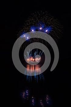 Orange fountain and blue stars fireworks over Brno`s Dam with lake reflection