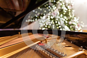 The grand piano interior with visible strings In the background a blurred Christmas tree, ornaments and lights