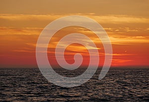 Orange gradient sky at dusk over ocean, just after sunset with dark waves below.