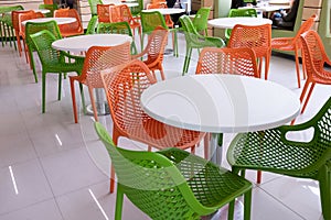 Orange and green chairs around white tables. A modern interior of food court in a mall, cafe, airport or family fast food