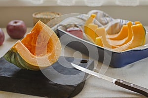 An orange-green pumpkin lies on a brown wooden cutting board and in a blue ceramic baking dish