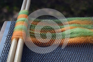 Orange and green wool roving on a blending board with two wooden dowels