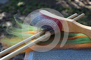 Orange and green wool roving on a blending board with two wooden dowels and a wire brush