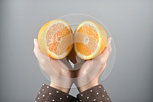 Orange half cut 2 pieces on women hands with brown coat on light grey background. horizontal image