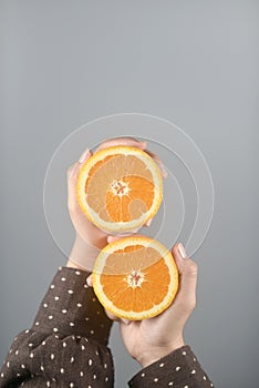 Orange half cut 2 pieces on women hands with brown coat on light grey background.vertical image