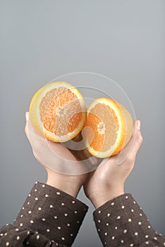 Orange half cut 2 pieces on women hands with brown coat on light grey background.vertical image