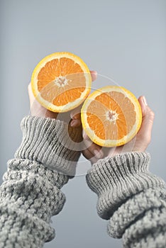 Orange half cut 2 pieces on women hands with sweater on light grey background. vertical image