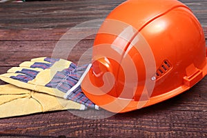 Orange hard hat and gloves for work on wood background.