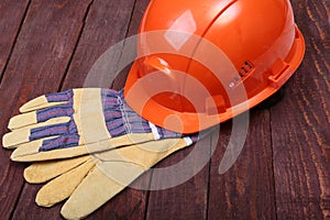 Orange hard hat and gloves for work on wood background.