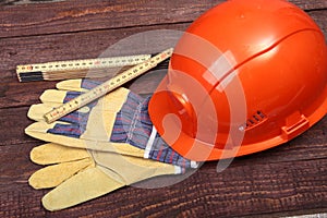 Orange hard hat and gloves for work on wood background.