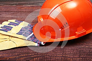 Orange hard hat and gloves for work on wood background.