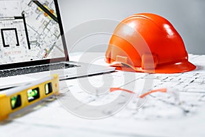 Orange hard hat, laptop  with drawings, level meter and protective glasses lying in a  blueprints on a table