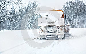 Orange highway maintenance gritter plough truck completely covered with snow, cleaning forest road, view from car