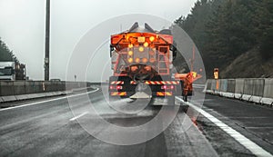 Orange highway maintenance gritter truck spreading de-icing salt, crystals dropping on the ice covered asphalt road during