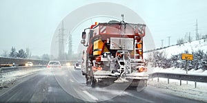 Orange highway maintenance gritter truck spreading de icing salt on road. Dangerous driving conditions