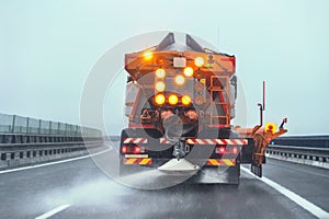 Orange highway maintenance gritter truck spreading de-icing salt on road in winter