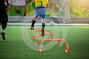 Orange hurdles markers on green artificial turf with blurry kid soccer is jumping cross it and coach is teaching him