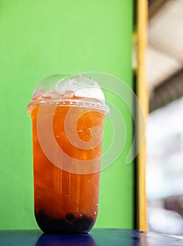 Orange iced tea in a clear plastic cup is placed near a green wall.