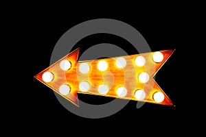 Orange illuminated display arrow sign with light bulbs against a seamless black background