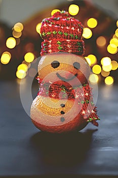 Orange illuminated by festive lights, arranged to resemble a snowman in a darkened setting