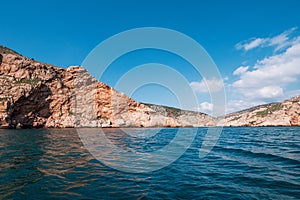 Orange island mountain coastline, blue sky with clouds and ocean water, summer travel landscape