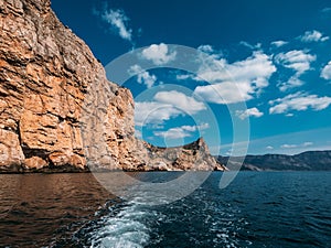 Orange island mountain coastline, blue sky with clouds and ocean water, view from boat, summer travel landscape