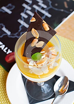 Orange Italian panna cotta served in a wine glass, with dark chocolate peanut and almond flakes