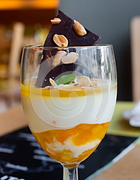 Orange Italian panna cotta served in a wine glass, with dark chocolate peanut and almond flakes