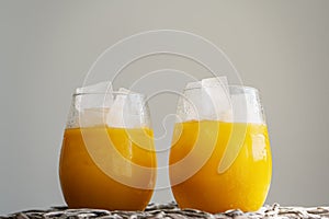 Orange juice or cocktail with ice in glass, cold summer lemonade on light gray background