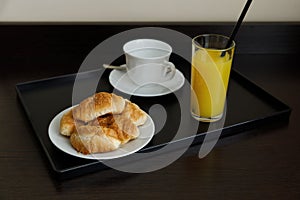Orange juice in a glass with croissants. Breakfast at the hotel, at home. The cup and saucer are white. The table is