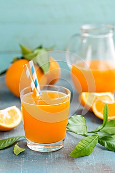 Orange juice in glass and fresh fruits with leaves on wooden background