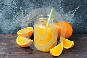 Orange juice in glass jar and fresh fruits oranges on dark background with copy space