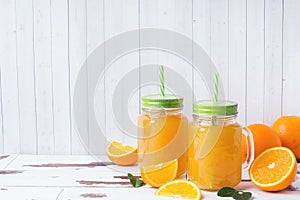 Orange juice in glass jars and fresh oranges on a white wooden rustic background
