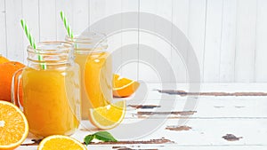 Orange juice in glass jars and fresh oranges on a white wooden rustic background