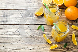 Orange juice in glass jars and fresh oranges on a wooden rustic background. Copy space